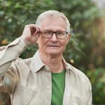 Senior man adjusting glasses in a sunny outdoor setting with greenery.