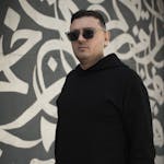 Stylish man in sunglasses posing against Arabic graffiti wall in Tehran.